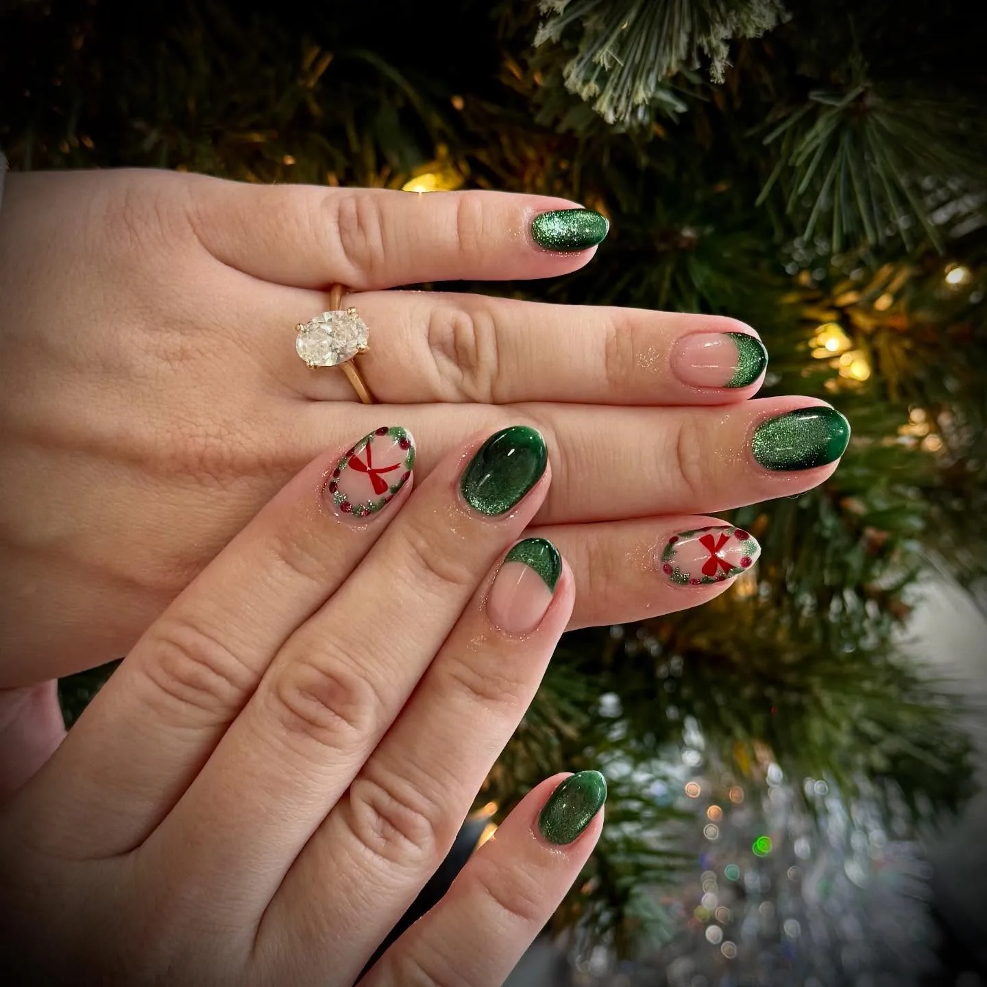 Short rounded nails in green glitter and velvety green, two with hand-painted wreaths and red bows, held up to a Christmas tree