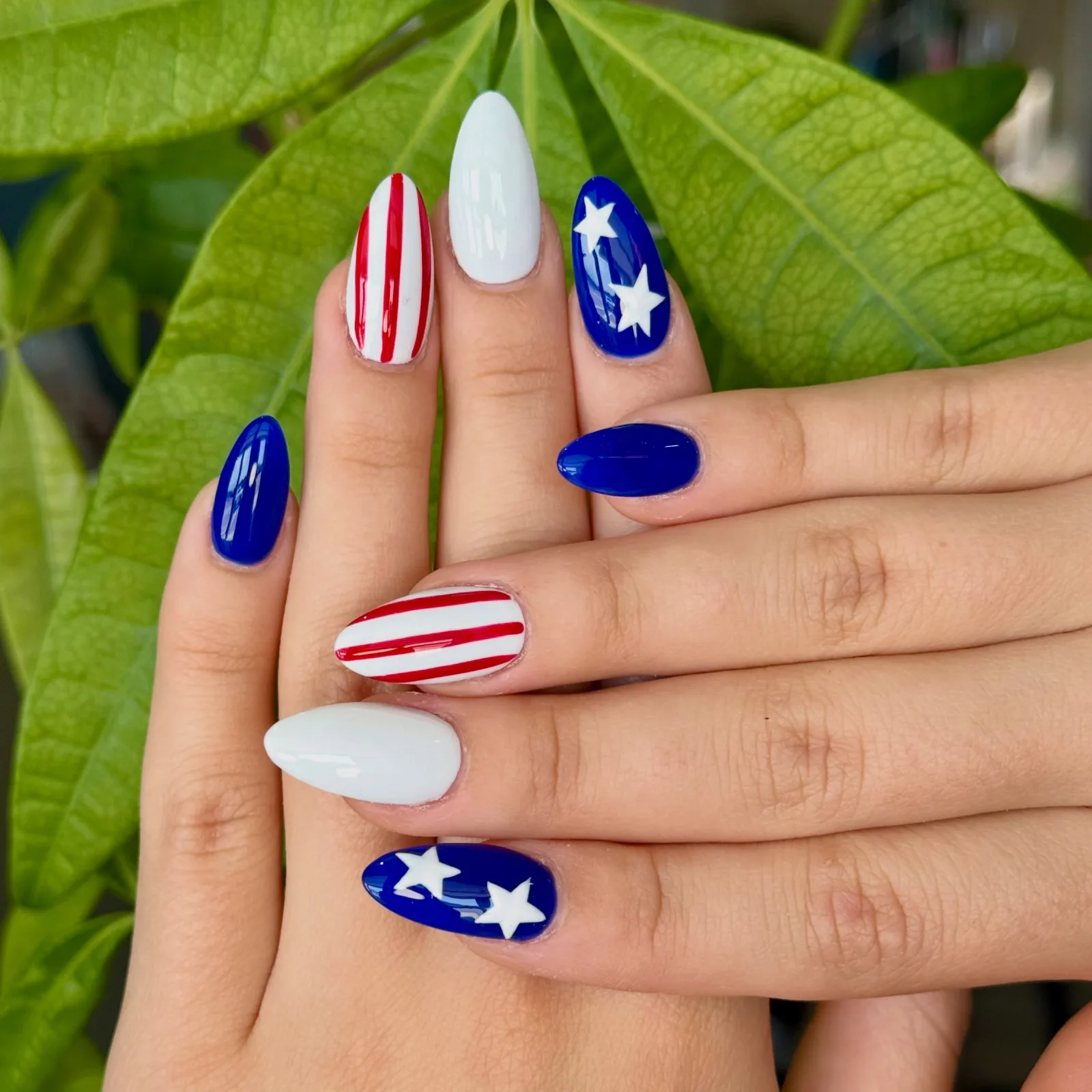 Almond nails painted as a flag: red and white stripes, plain white, and royal blue with white stars