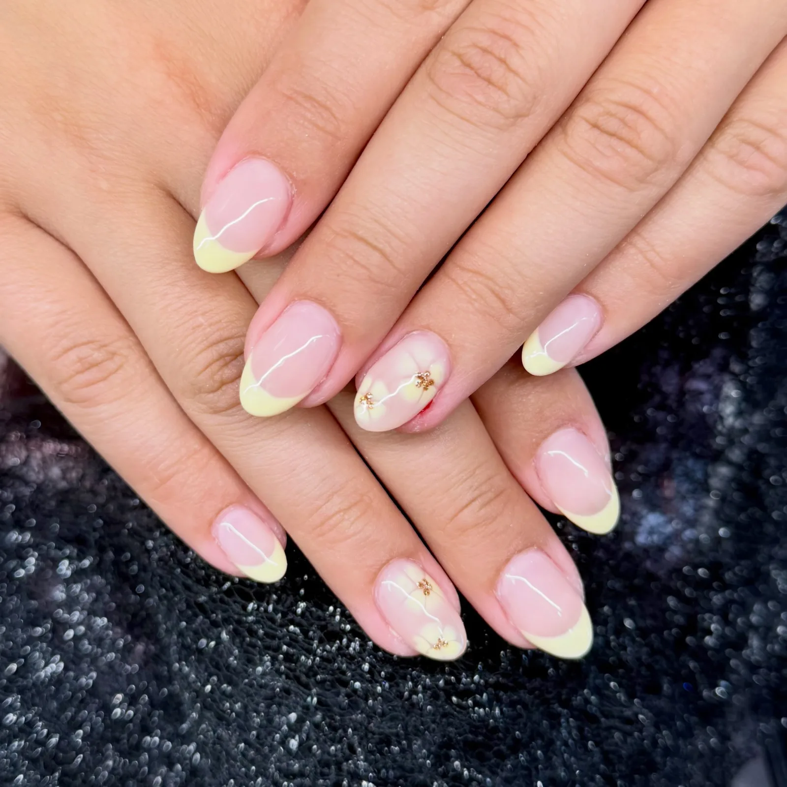 Almond nails with pale yellow French tips, two with soft yellow flowers and gold centers